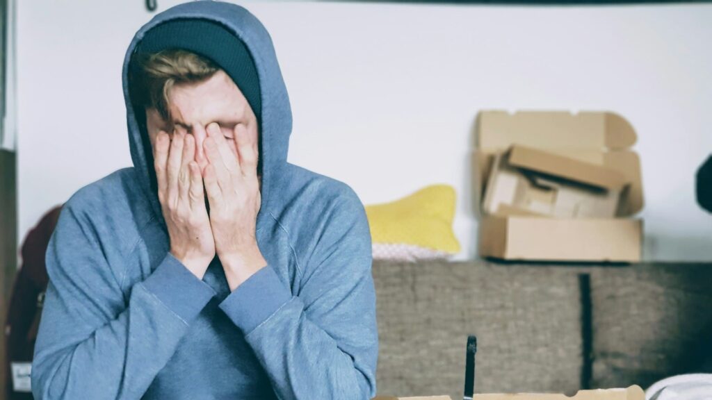 Gestreste man zit met handen voor zijn gezicht in rommelige kamer – focus op hygiëne en zelfzorg